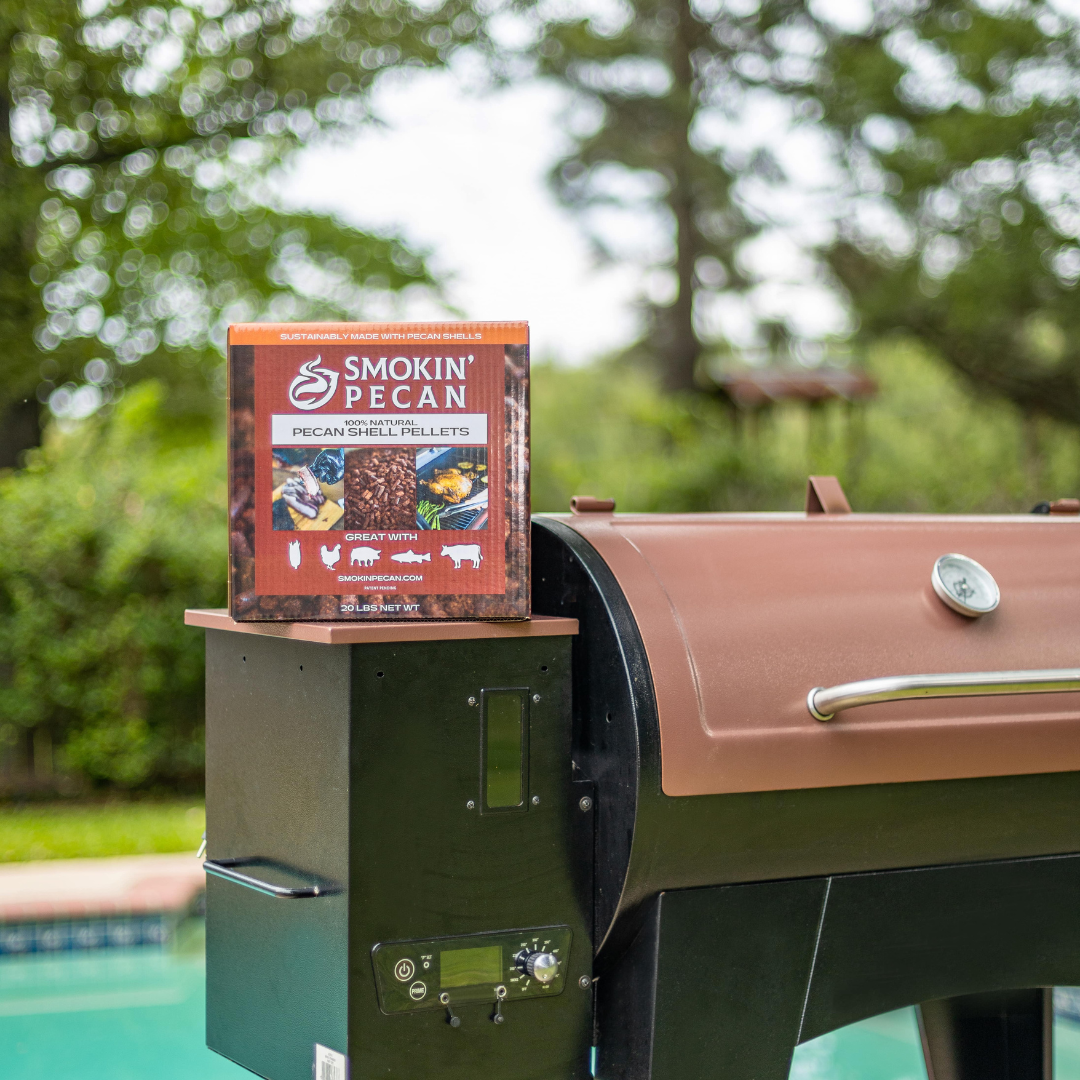 A 20 lb box of Smokin' Pecan Pecan Shell Pellets sits on a black and brown grill by a backyard pool, showcasing this eco-friendly barbecue fuel.