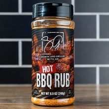 A jar of AB's Hot BBQ Rub by Smokin and Grillin wit AB rests on a wooden surface before black tiles. The label displays grilled meat with bold white and red text, highlighting the smoky, spicy flavor of this barbecue seasoning.