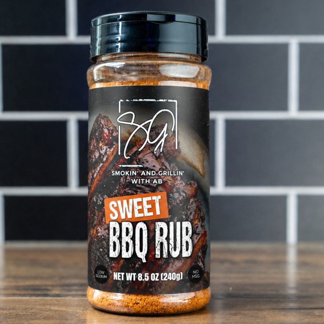 A jar of AB's Sweet BBQ Rub from Smokin and Grillin wit AB rests on a wooden surface with a black and white tiled background. The label shows grilled meat and indicates a net weight of 8.5 oz (240g).