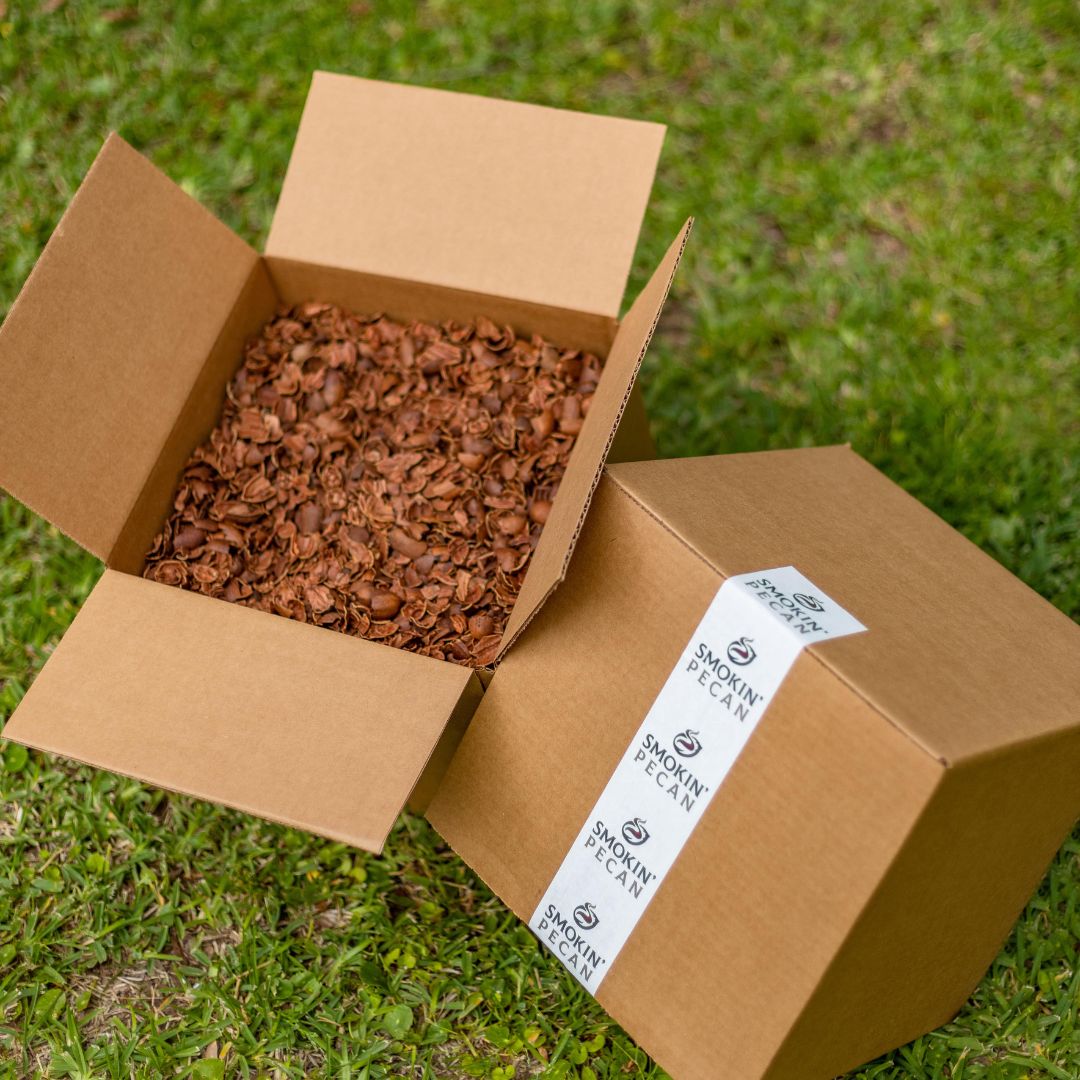 A 17 lb box of Smokin' Pecan Shells (Just Shells) sits open on grass, perfect for smoking meat, with a sealed Smokin' Pecan box beside it.