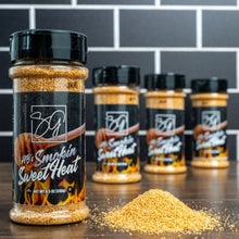 A plastic bottle of AB’s Sweet Heat — Sweet, Smoky All-Purpose Seasoning with a black label featuring flames, standing next to a small pile of golden spices, with three additional bottles blurred in the background.