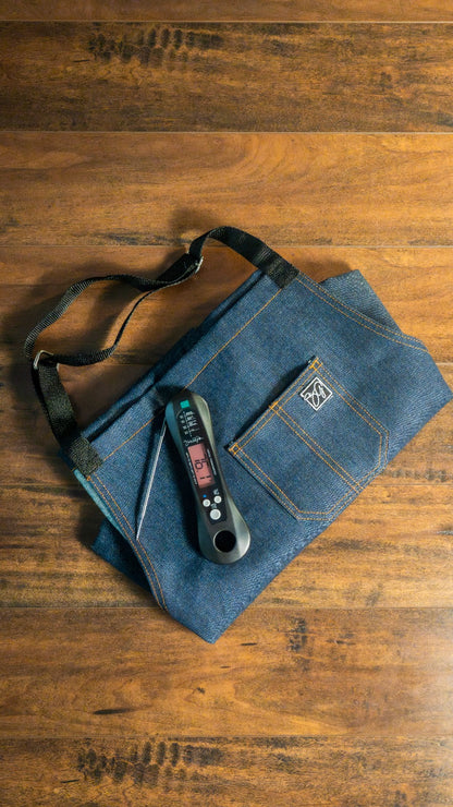 The Smokin and Grillin wit AB Kitchen Bundle features a digital food thermometer and stainless steel probe, displayed on a folded denim apron with black straps—a must-have set for precise cooking.
